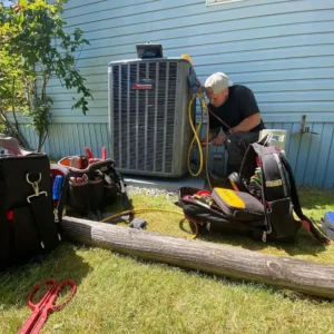 Technician repairing an air conditioning unit beside tool bags on grass.